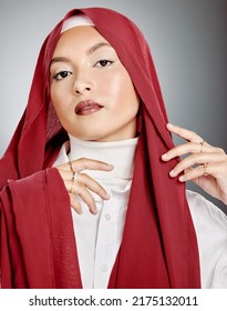 Portrait Of A Woman Wearing A Red Hijab Against Grey Studio Background And Copyspace. Young Muslim Lady Wearing A Headscarf, Posing And Showing Radiant Skin, Makeup, Eyelash Extensions And Jewellery