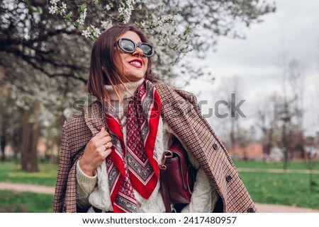 Portrait of woman wearing red scarf and sunglasses in spring park holding purse. Retro female fashion. Old money