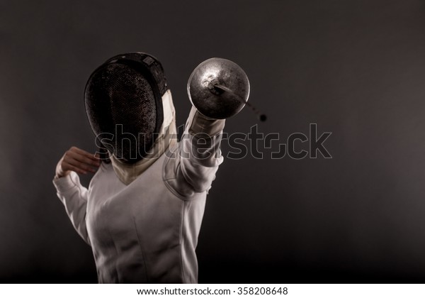 Portrait of woman wearing white fencing costume\
practicing with the\
sword.