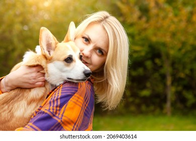 Portrait of a woman with a welsh corgi dog. Beautiful blonde woman with her beloved pet, looking at the camera. Natural autumn background. The concept of an active lifestyle with a pet.