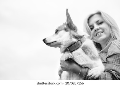 Portrait of a woman with welsh corgi dog. Beautiful blonde woman with her beloved pet, looking at the camera against the sky. The concept of an active lifestyle with a pet. Black and white.
