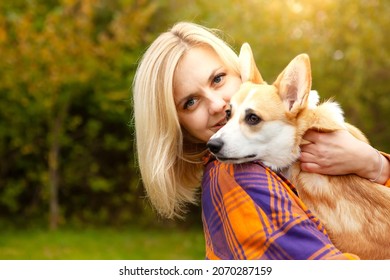 Portrait of a woman with a welsh corgi dog. Beautiful blonde woman with her beloved pet, looking at the camera. Natural autumn background. The concept of an active lifestyle with a pet.