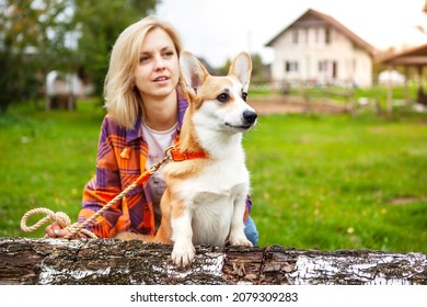 Portrait of a woman with a welsh corgi dog. Beautiful blonde woman with her beloved pet, looks into the distance. Against the background of the garden and country house. Active lifestyle with a pet.