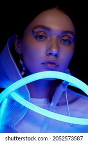 Portrait Of Woman In White Transparent Raincoat And Flexible Blue Neon Tube Light. Black Background                                              