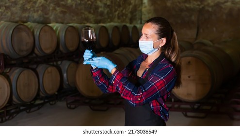 Portrait Of Woman Winemaker Wearing Protective Face Mask Examining Wine In Glass At Winery