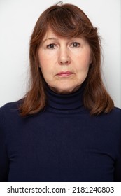 Portrait Of A Woman Without Retouching Sitting On A Light Solid Background. An Elderly Beautiful Woman In A Dark Sweater Looks Into The Frame

