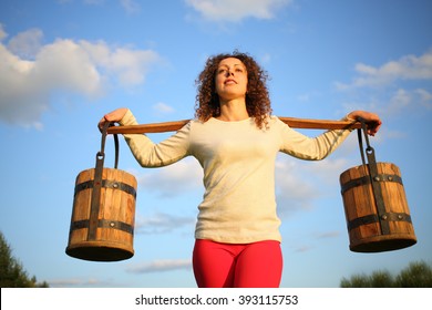Portrait of a woman with a yoke and wooden pails against the blue sky - Shutterstock ID 393115753