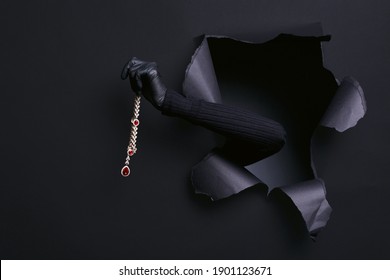 Portrait of woman`s hand in black sweater steals a diamond necklace through a ripped studio background