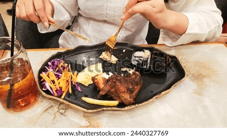 portrait of a woman's hand stabbing khubus (pita bread) accompanied by oven-roasted chicken, typical Arabic food with a fork and knife on a plate at a 45 degree angle