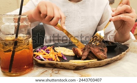 portrait of woman's hands slicing oven roasted chicken accompanied by khubus (pita bread) typical Arabic food with a fork and knife on a plate