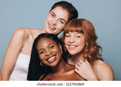 Portrait of women with different skin tones smiling at the camera in a studio. Group of happy young women feeling comfortable in their own skin. Three body positive young women standing together.