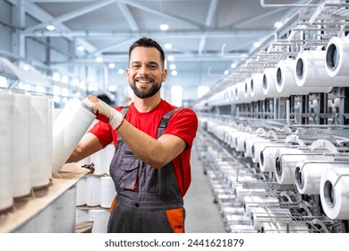 Portrait of worker holding thread spool inside textile factory. In background industrial knitting machine. - Powered by Shutterstock