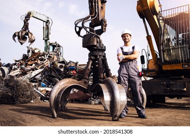 Portrait of worker standing by hydraulic industrial machine with claw attachment used for lifting scrap metal parts in junk yard. - Powered by Shutterstock