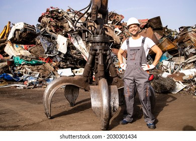 Portrait of worker standing by hydraulic industrial machine with claw attachment used for lifting scrap metal parts in junk yard. - Powered by Shutterstock