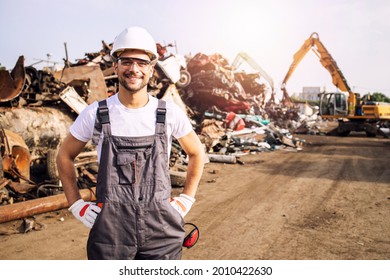 Portrait of worker standing in metal junk yard with crane lifting scrap metal for recycling. - Shutterstock ID 2010422630