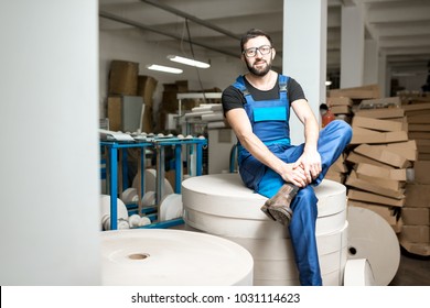 Portrait Of A Worker In Uniform Sitting On The Big Paper Rolls At The Packaging Manufacturing