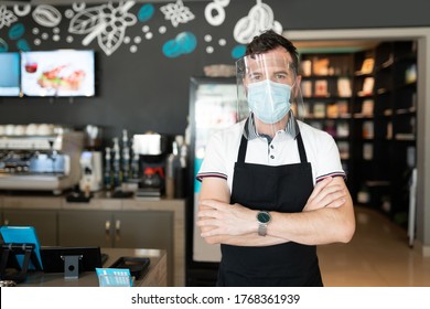 Portrait Of Worker Wearing Face Shield And Mask Standing In Cafe With Arms Crossed