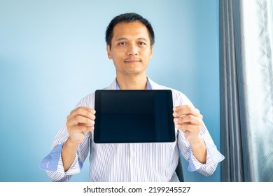 Portrait, A Working Asian Man, Aged 45 Years And Over, Sitting In A Modern-style Office. Both Hands Holding An Ipad Which Has Blank Black Screen Space, Business Concept Isolated Light Blue Background