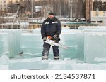 Portrait of a working assembler in a blue jacket and a knitted black hat near an ice panel with a chainsaw