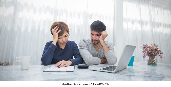 Portrait Of Worried Couple Paying Bills Online Via Laptop In Living Room. Young Man Woman With Computer Checkbook Worrying About Expense Bills, Hands Holding Head. Stressful Financial Problem Concept