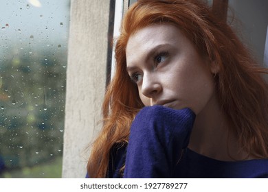 Portrait of worried girl looking through the window at home