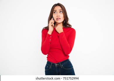 Portrait Of A Worried Scared Asian Woman Talking On Mobile Phone While Standing And Looking Away Isolated Over White Background