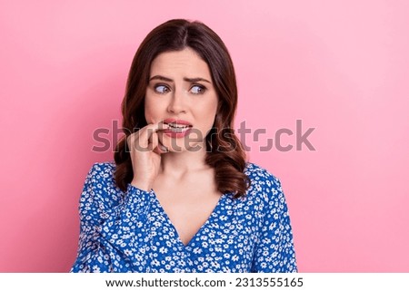 Portrait of worried stressed frightened pretty girl wear blue clothes biting finger look empty space isolated on pink color background