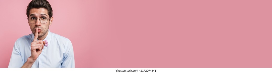 Portrait Of A Worried Young Brunette Nerd Man Wearing Shirt And Bowtie Standing Over Pink Wall Background Showing Silence Gesture