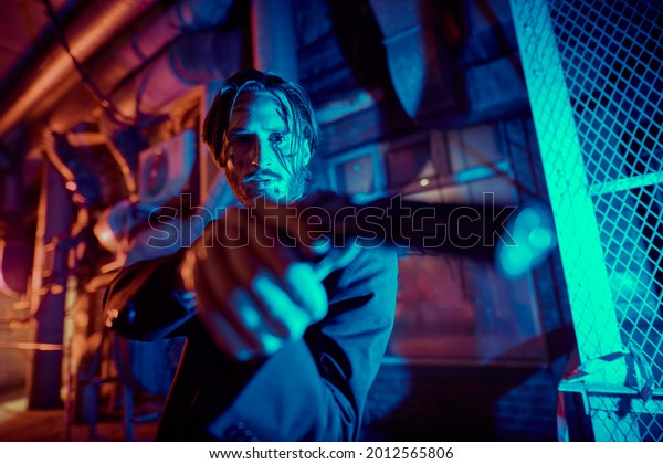 Portrait of a wounded action hero man aiming a gun\
in the light of the night city.\
