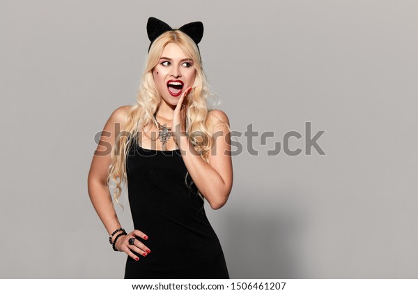 portrait of wow sexy young woman\
in black witch halloween costume with cat ears in black dress on\
party over gray background. the concept of Halloween . funny\
face