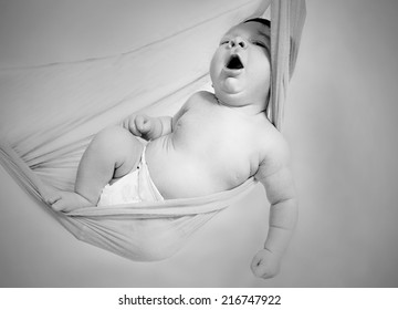 Portrait Of A Yawning Newborn Baby In Hammock In Black And White Shallow DOF