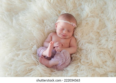 Portrait Of A Yawning Ten Day Old Newborn Baby Girl. She Is Curled Up And Sleeping On Her Back On A Cream Colored Flokati Rug.