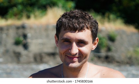 Portrait Of Yiung Man On The Beach. Cheerful Sunburnt Man Smiling And Squinting Enjoying Long Warm Vacation.