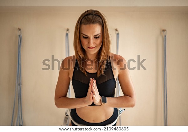 Portrait of yogi woman with namaste hands\
position in dog face up hanged on rope. Sports female practicing\
fly yoga Iyengar therapy at gym with props inventory. Fitness lady\
harmony healthy\
balance