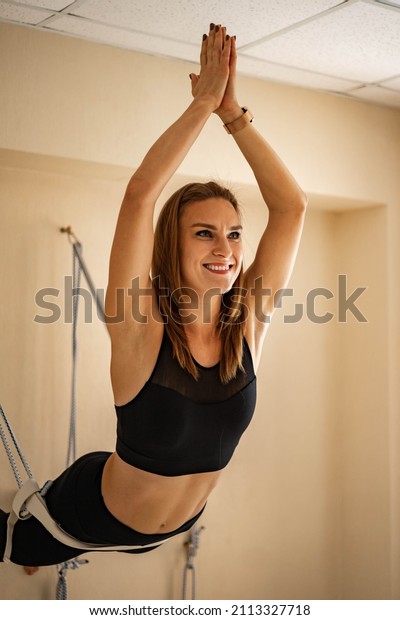 Portrait of yogi woman with namaste hands\
position in dog face up hanged on rope. Sports female practicing\
fly yoga Iyengar therapy at gym with props inventory. Fitness lady\
harmony healthy\
balance