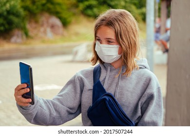 Portrait Of Young 12 Year Old Caucasian Girl Wearing White Face Mask And Grey Hoodie Taking A Selfie Outdoors