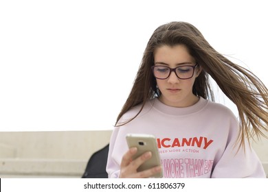 Portrait Of A Young 15 Year Old Teenage Girl Sitting Looking At Her Mobile Phone.