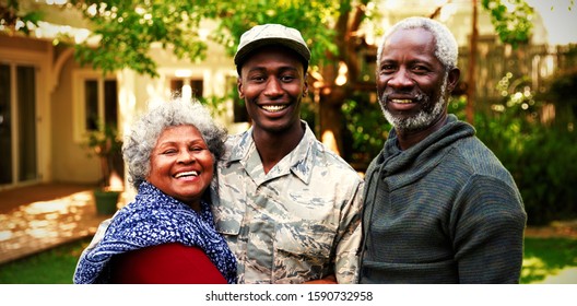 Portrait of a young adult African American male soldier in the garden outside his home embracing with his parents, all of them smiling to camera