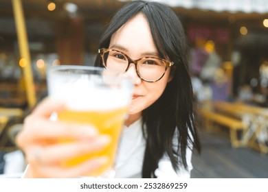 Portrait of young adult asian woman with eyeglasses drinking beer at restaurant outdoor area. People relax in city break concept. - Powered by Shutterstock