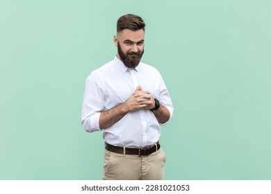 Portrait of young adult bearded businessman wearing white shirt looking at camera with cunning tricky face and smirk, planning evil trick. Indoor studio shot isolated on light green background.
