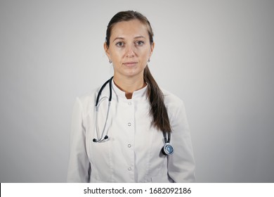 Portrait Of Young Adult Female Doctor Wearing Medical Coat And Stethoscope On Her Neck Looking Straight To The Camera. Isolated Background