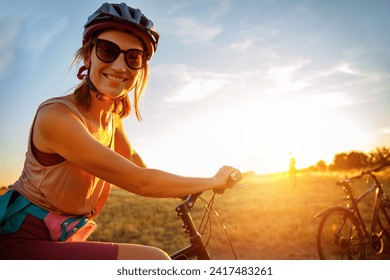 Portrait of young adult fit sporty smiling caucasian woman enjoy riding cross country bike on hay dry field in warm sunset sunlight evening morning. Healthy recreation lifestyle leisure time - Powered by Shutterstock