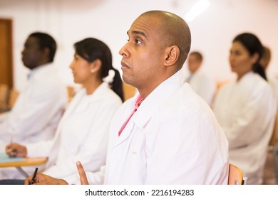 Portrait Of Young Adult Male Doctor Attentively Listening To Lecture With Colleagues At Medical Conference