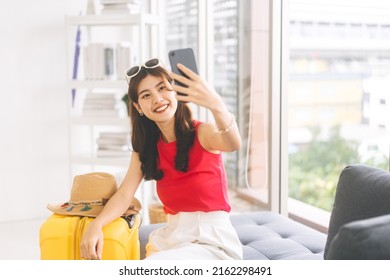 Portrait of young adult southeast asian woman with yellow travel luggage. Using smartphone for selfie before start journey. Getting ready for travel trip at home concept.