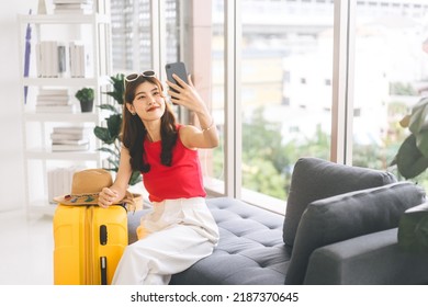 Portrait Of Young Adult Southeast Asian Woman With Yellow Travel Luggage. Using Smartphone For Selfie Before Start Journey. Getting Ready For Travel Trip At Home Concept.