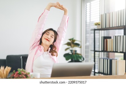 Portrait Of Young Adult Southeast Business Asian Woman Stretching Hand For Relax Break Time At Work Place. Wearing Casual Pink Shirt Sitting In Home Office.