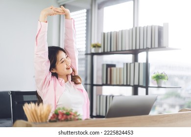 Portrait Of Young Adult Southeast Business Asian Woman Stretching Hand For Relax Break Time At Work Place. Wearing Casual Pink Shirt Sitting In Home Office.