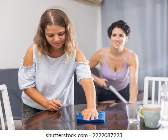 Portrait Of Young Adult Woman Keeping Home Clean Together With Her Wife, Dusting Table And Hoovering