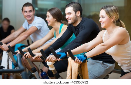 Portrait of young adults working out of cycling in modern fitness club . Selective focus