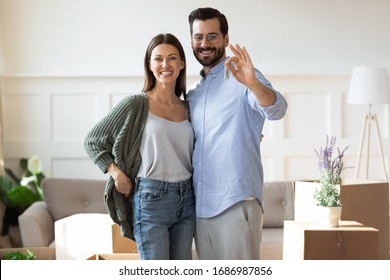 Portrait of young affectionate couple embracing, showing keys to camera. Happy man in glasses cuddling pretty wife, excited by moving into new apartment. Smiling homeowners satisfied with real estate.